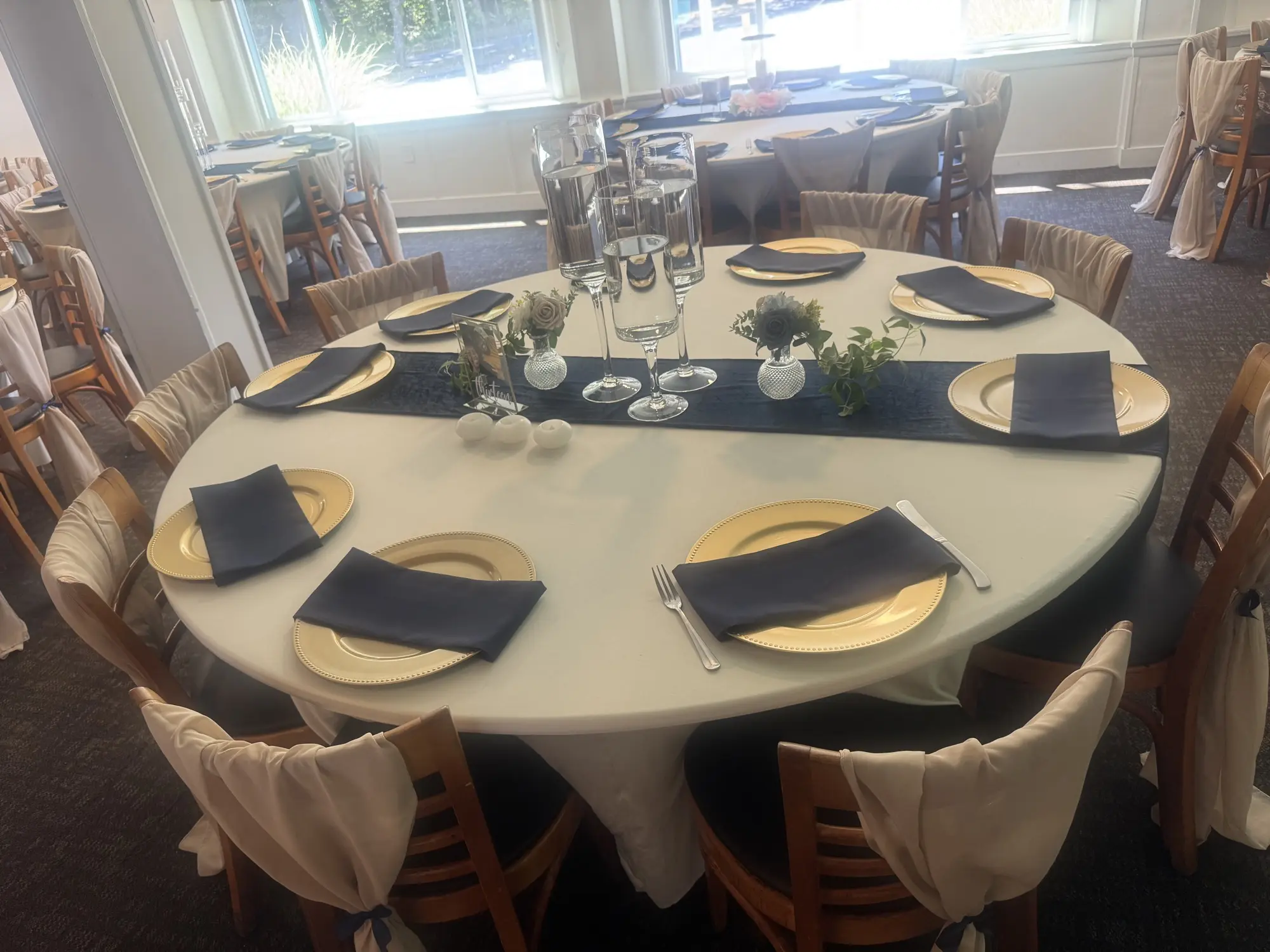 Round table with white linens, gold chargers, navy napkins, and floral centerpiece at Barnard Hall