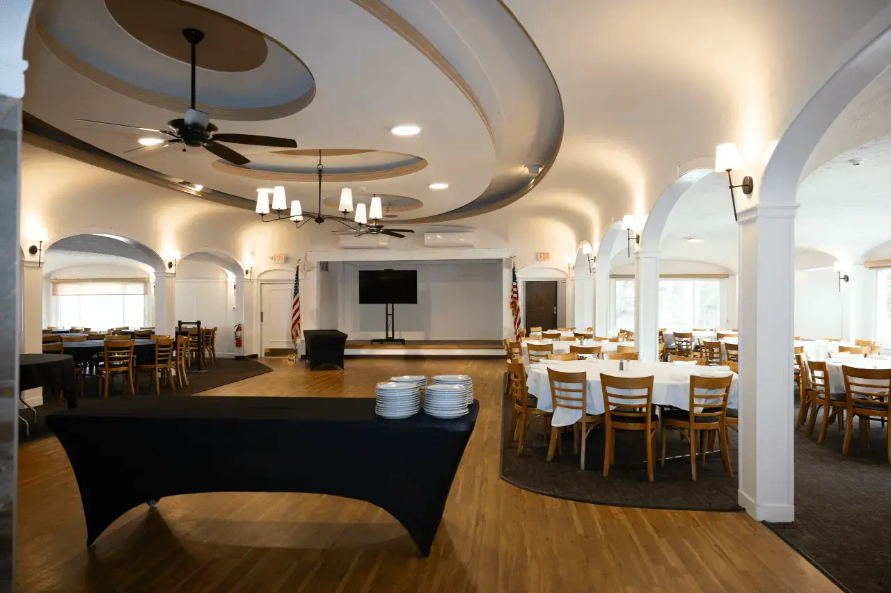 Barnard Hall ballroom with arched ceiling, circular dining tables, stage with large screen and American flags